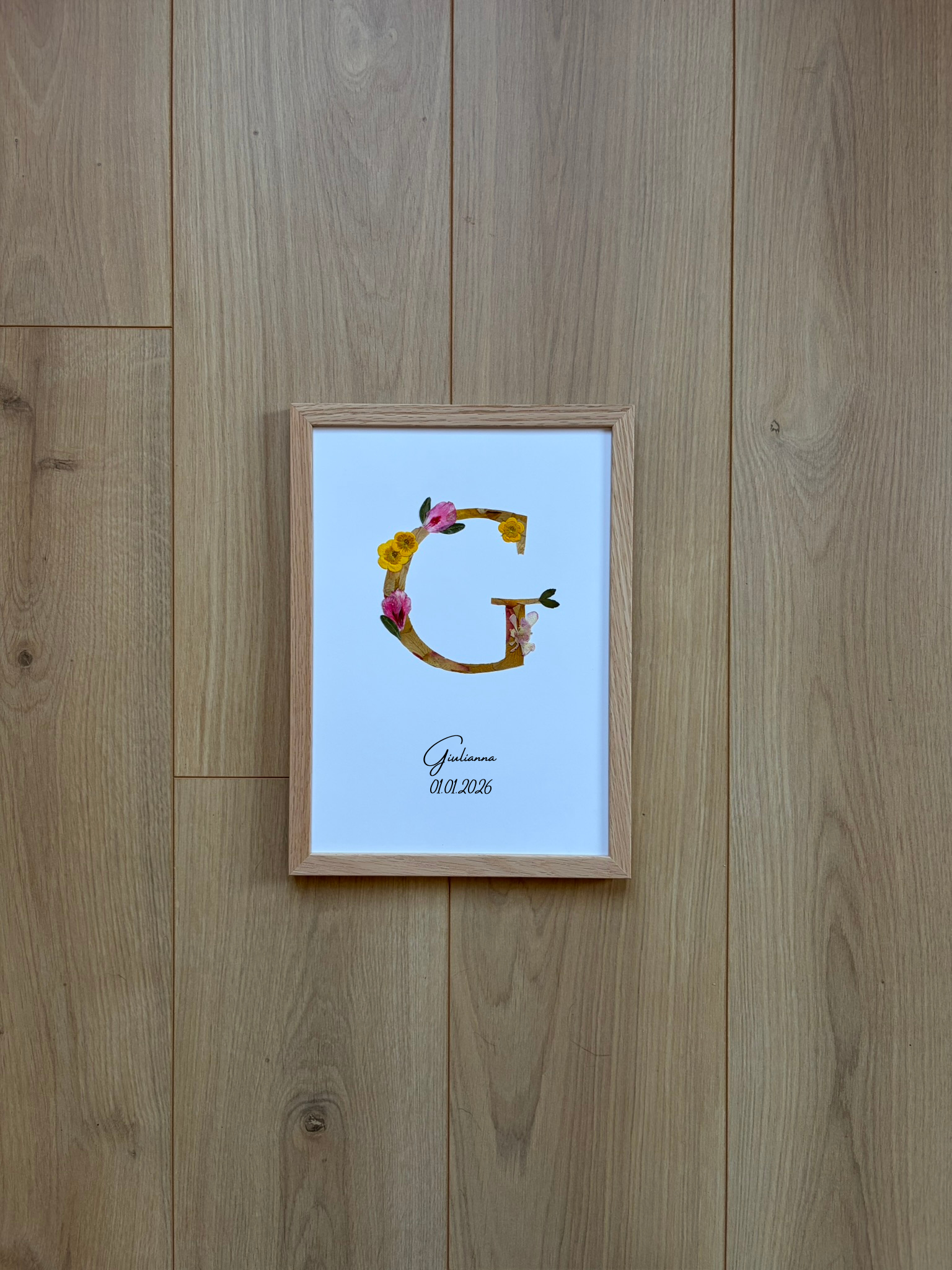 n monogramme floral réalisé à la main à partir de véritables fleurs pressées. La lettre G, délicatement composée de pétales roses et jaunes, est encadrée de bois naturel pour une finition douce et épurée. Personnalisé avec le prénom Giulianna et sa date de naissance, ce cadre devient un souvenir unique et intemporel, parfait pour célébrer une naissance avec poésie.