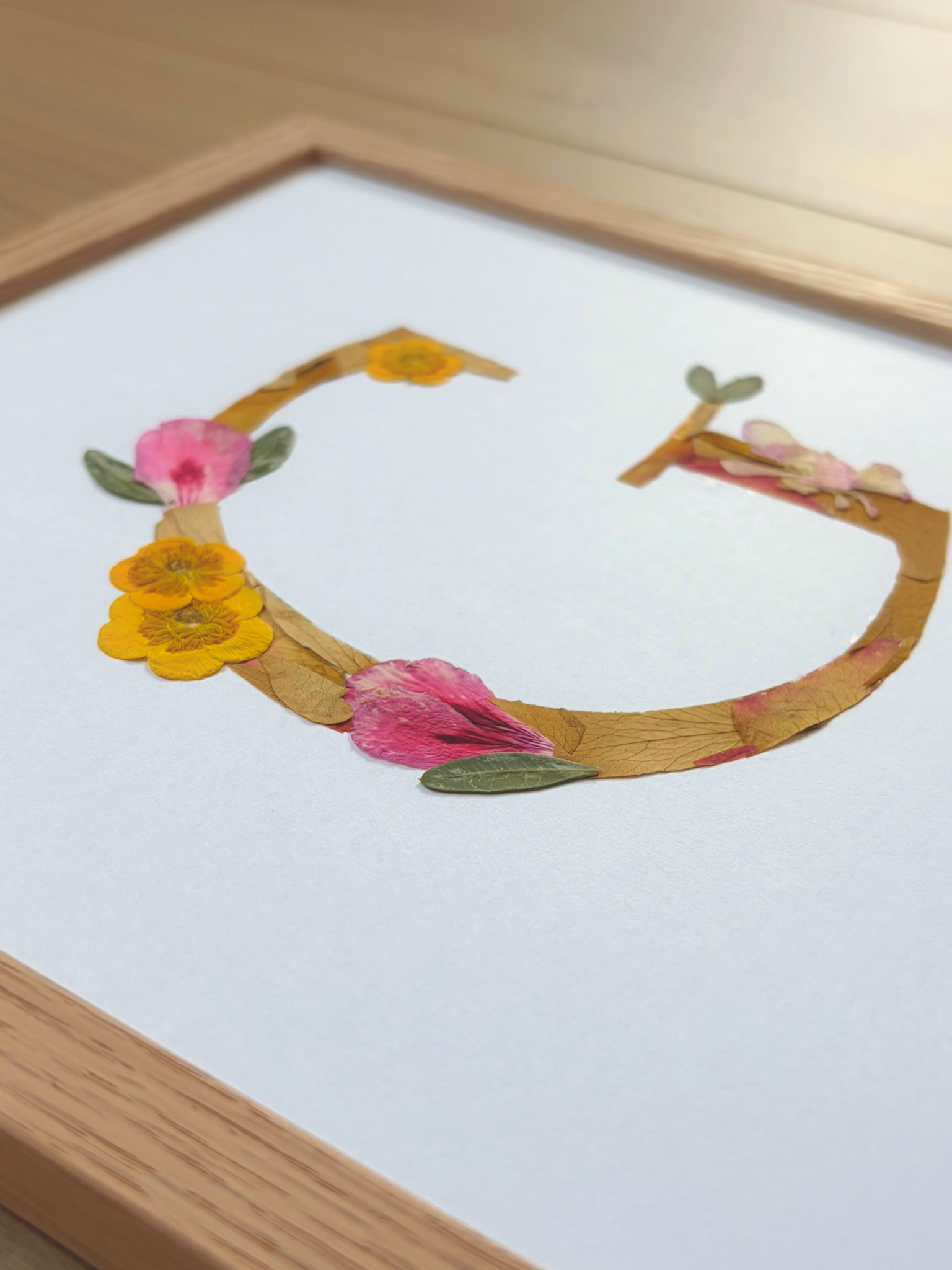 n monogramme floral réalisé à la main à partir de véritables fleurs pressées. La lettre G, délicatement composée de pétales roses et jaunes, est encadrée de bois naturel pour une finition douce et épurée. Personnalisé avec le prénom Giulianna et sa date de naissance, ce cadre devient un souvenir unique et intemporel, parfait pour célébrer une naissance avec poésie.